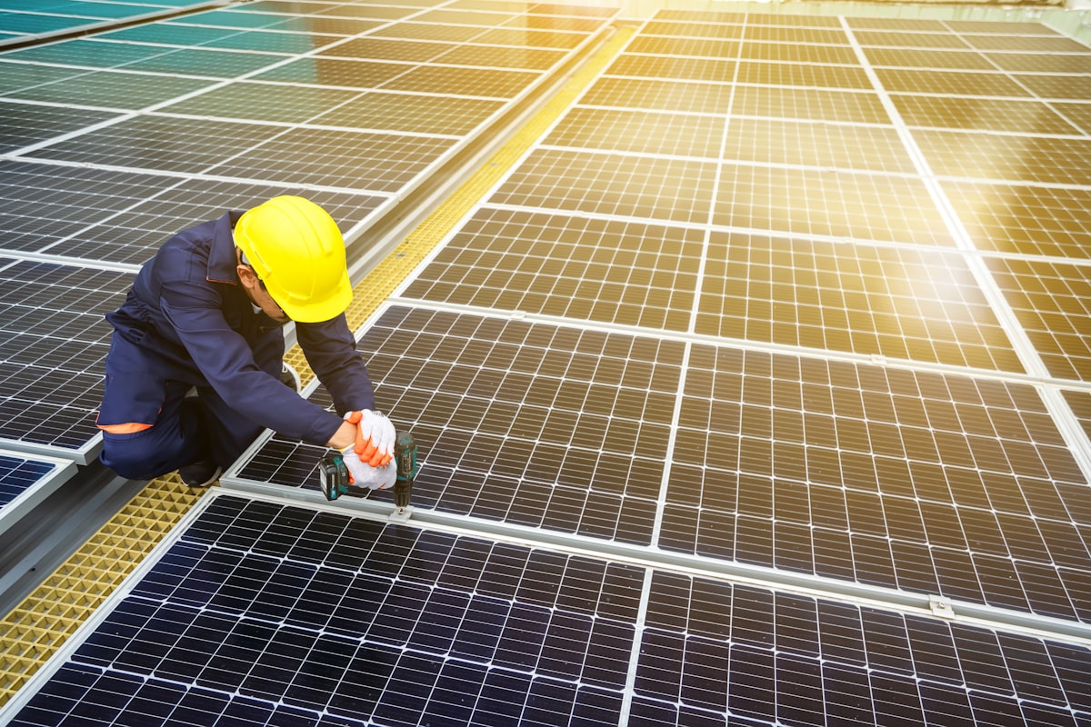 A solar technician bolting panels onto a large rooftop array